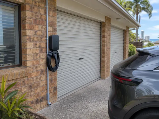 Wall-mounted EV charger with coiled cable on a brick garage wall beside a driveway in Coolangatta