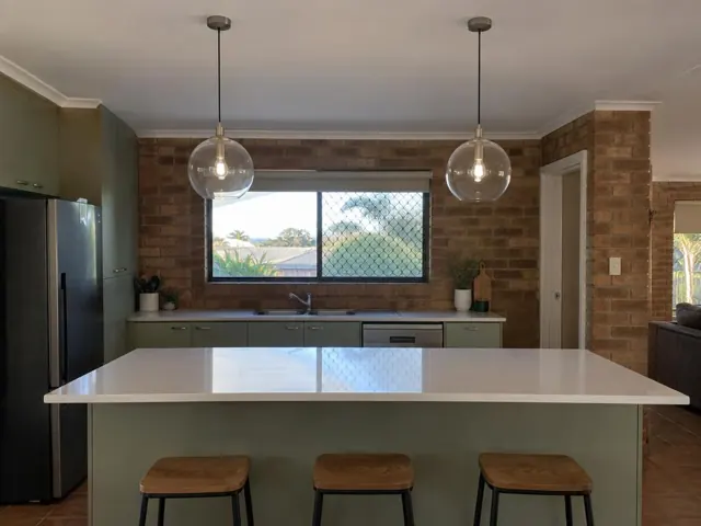 Kitchen with two glass pendant lights above an island, brick walls and green cabinets in Tugun